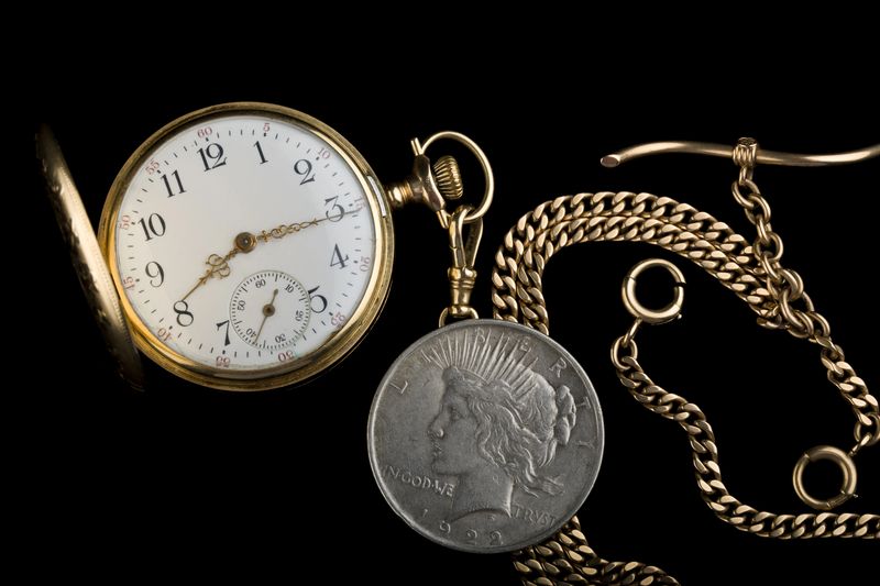 1922 Peace silver dollar beside an antique gold pocket watch, the kind of heirloom Dallas families bring to a coin dealer